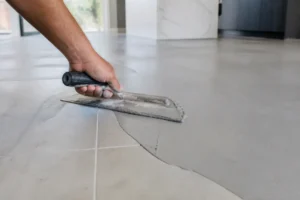 Application de béton ciré sur carrelage existant par un artisan, gros plan sur les mains et l'outil.