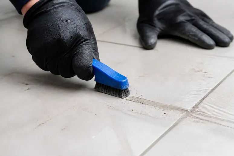 Mains gantées utilisant une brosse à joints pour un frottage minutieux.