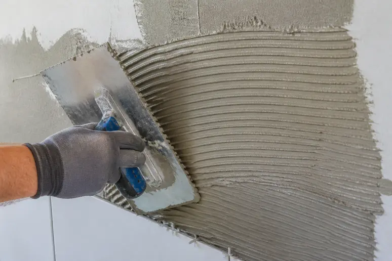 Application de colle carrelage flex avec une spatule dentée pour une pose uniforme.