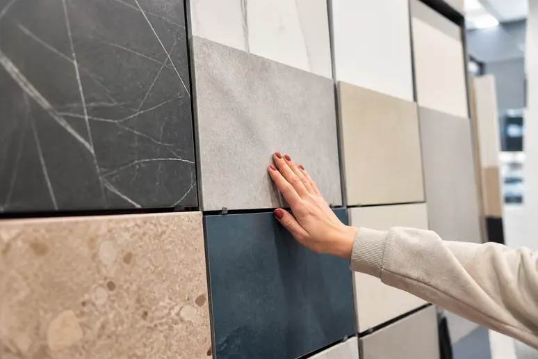 Choix de carrelage cuisine effet pierre et marbre, une main examine les textures disponibles.