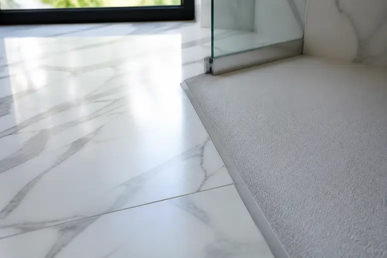 Transition entre un sol de salle de bain en carrelage marbre blanc et la zone de douche.