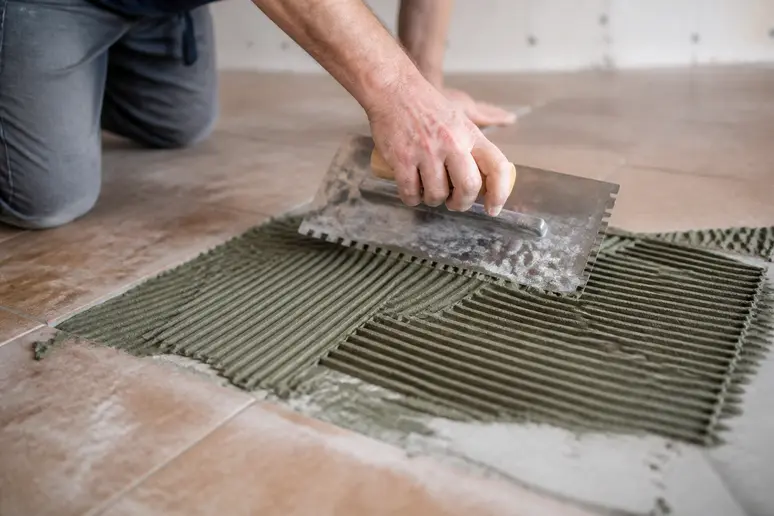 Application de colle pour coller du carrelage sur du carrelage avec une spatule crantée.