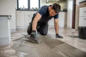 Artisan appliquant de la colle pour carreler sur un ancien carrelage mural, prêt pour une nouvelle pose.
