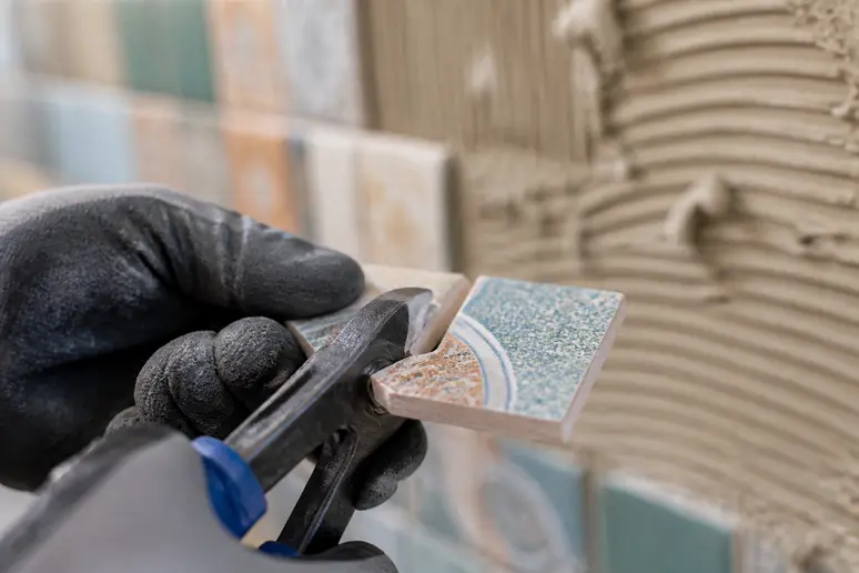 Détail d'un carreleur coupant avec précision des émaux de Briare pour une mosaïque.