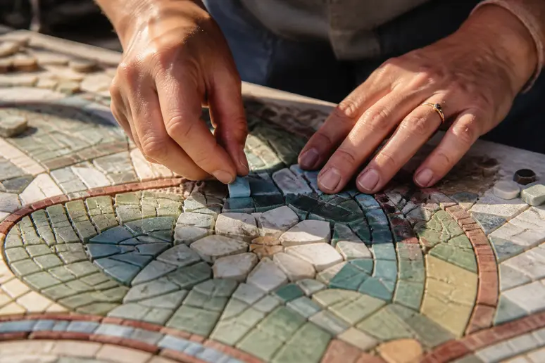 Mains d'une artiste réalisant une mosaïque avec des émaux de Briare déclassés aux nuances variées.