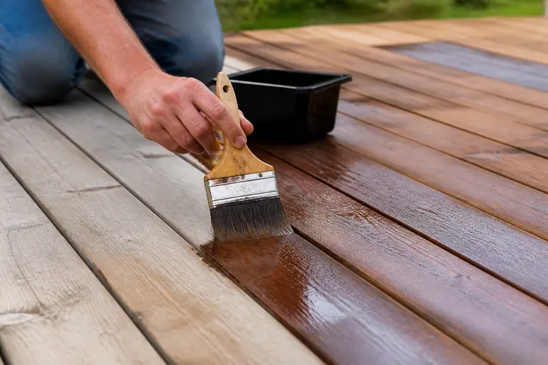 Application d'un saturateur protecteur sur les lames d'une terrasse en bois avec une large brosse
