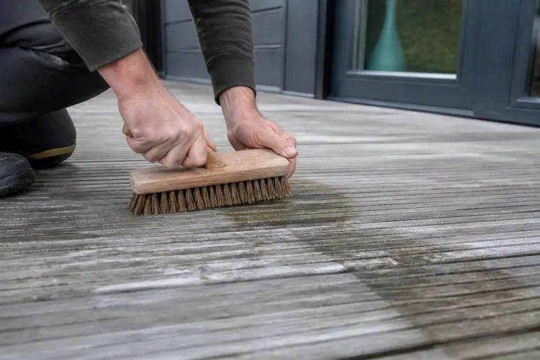 Brossage minutieux des fibres d'une terrasse en bois après application d'un produit dégriseur