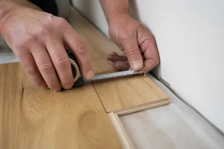 Mesure de l'espace de dilatation d'un parquet avec un mètre ruban le long d'un mur