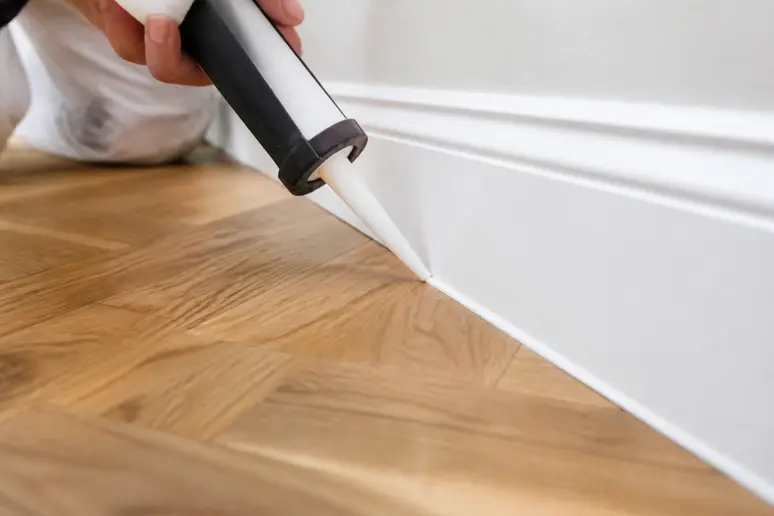 Application d'un mastic acrylique au pistolet pour la finition des joints de parquet