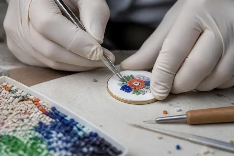 Des mains expertes placent avec minutie des tesselles colorées pour une micro mosaïque sur un bijou.