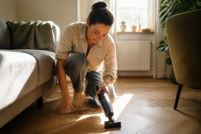 Une femme nettoie son parquet avec un aspirateur muni d'une brosse douce pour un dépoussiérage efficace.