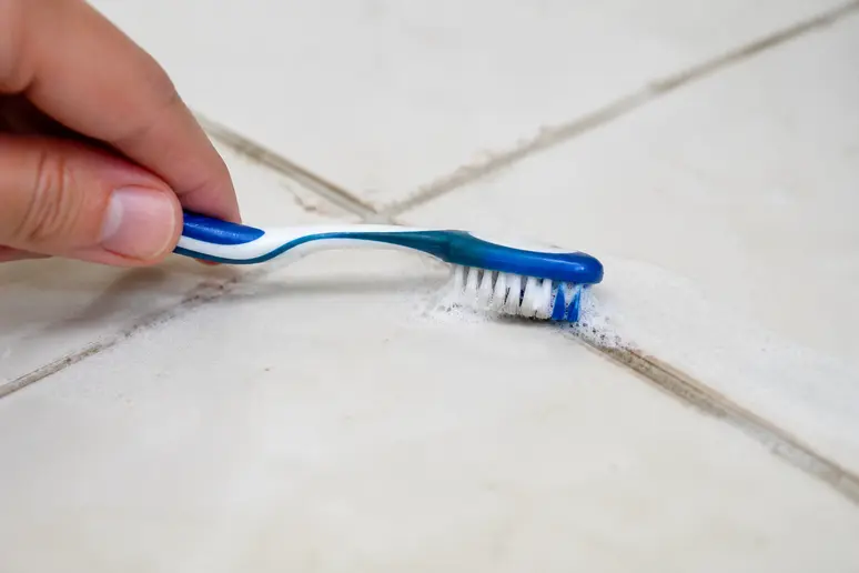 Brosse à dents nettoyant les joints d'un carrelage avec du bicarbonate.