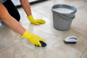 Mains gantées nettoyant en profondeur un carrelage avec une brosse et de l'eau savonneuse.