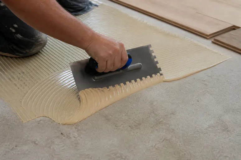 Application de la colle en plein sur le support avant la pose du parquet collé