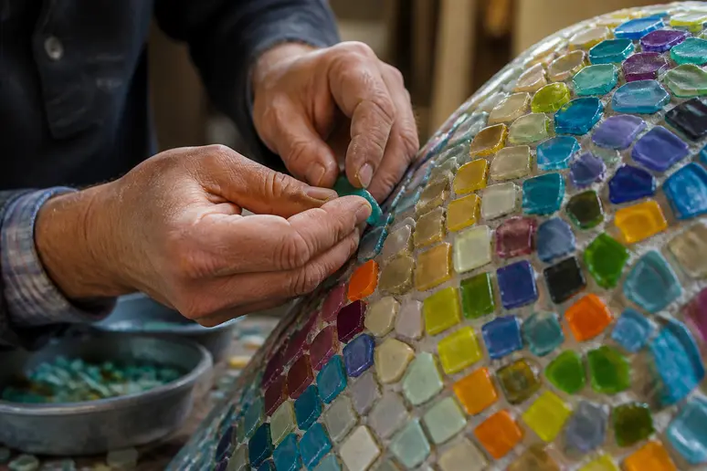 Pose minutieuse de pâte de verre mosaïque colorée sur une surface courbe par un artisan expérimenté.