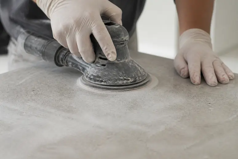 Mains ponçant un carrelage de salle de bain pour préparer la peinture : étape clé pour peindre du carrelage salle de bain.