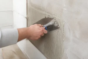 Main d'un bricoleur expérimenté en train de poser du carrelage sur un mur avec une truelle.