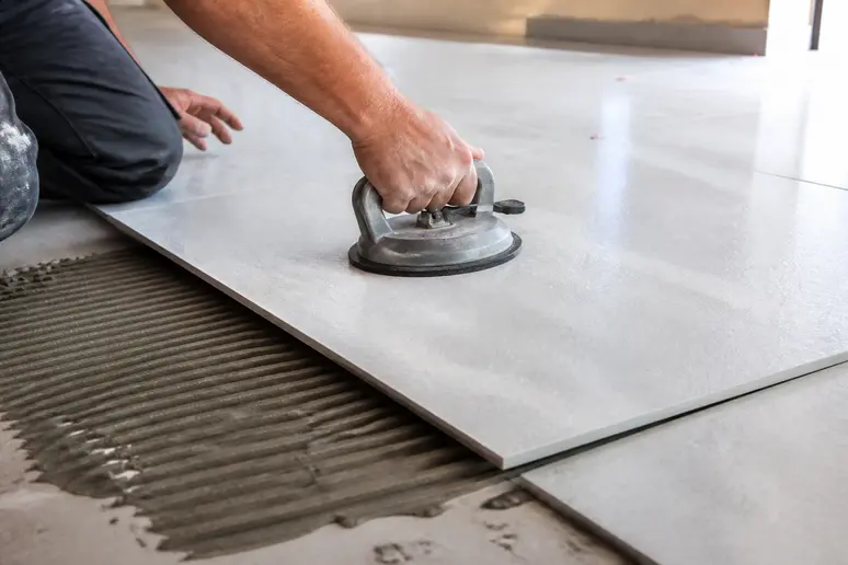 Mains d'un artisan utilisant une ventouse pour poser un grand carreau, illustrant le prix d'une pose de carrelage.