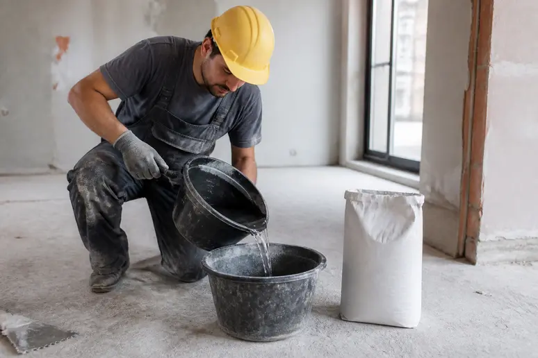 Ouverture d'un sac de colle carrelage de 25 kg sur un chantier de rénovation.