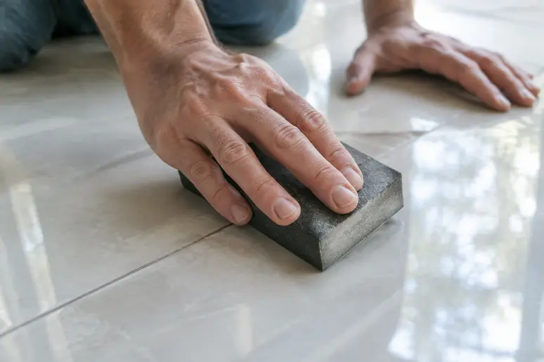 Ponçage léger d'un carreau de carrelage au sol avec une cale abrasive avant peinture.