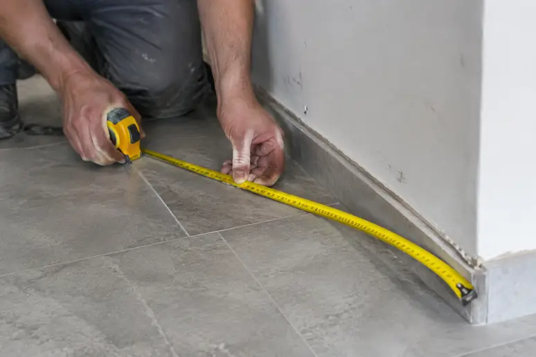 Mesure au mètre ruban d'une surface au sol pour calculer m2 carrelage dans une pièce.