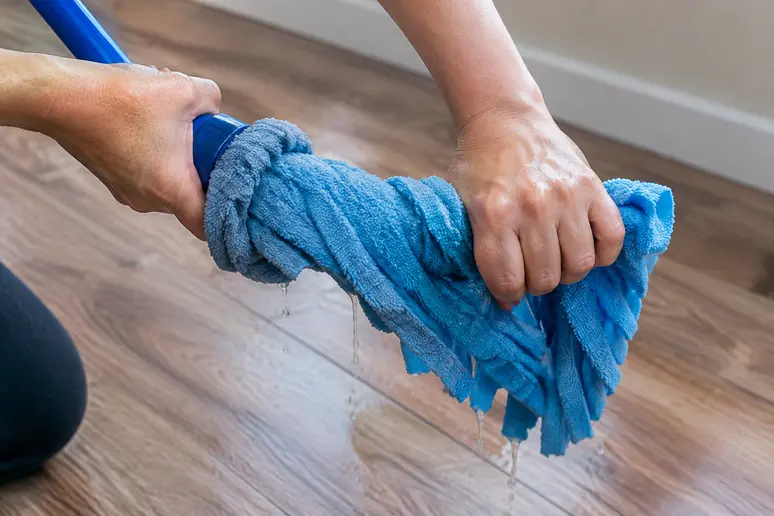 mains essorant fermement une microfibre pour nettoyer un parquet flottant sans excès d'eau