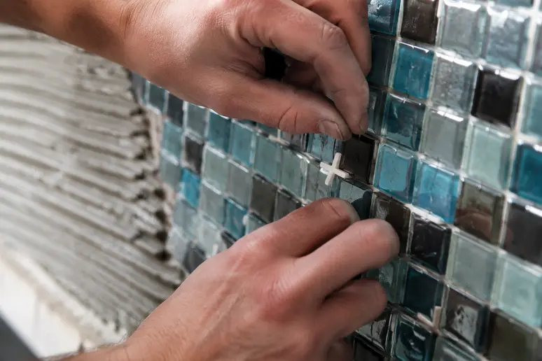 Mains posant des croisillons entre des plaques de mosaïques pour garantir un espacement régulier