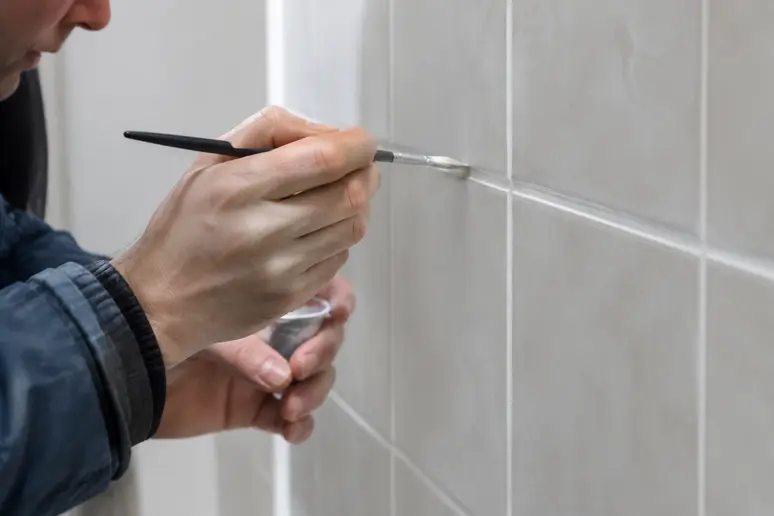 Application minutieuse de peinture sur les joints de carrelage avec un pinceau fin