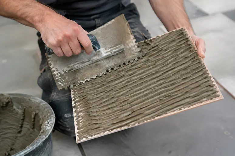 Application du mortier-colle à la trantane sur une plinthe carrelage avec un peigne dentelé.